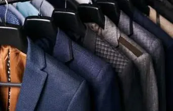 Řada obleků visících na háčcích v šatníku.