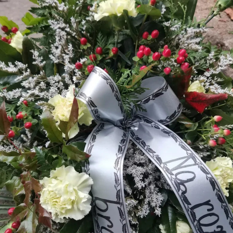 Smuteční věnec s bílými růžemi a stříbrnou stuhou s černým nápisem.