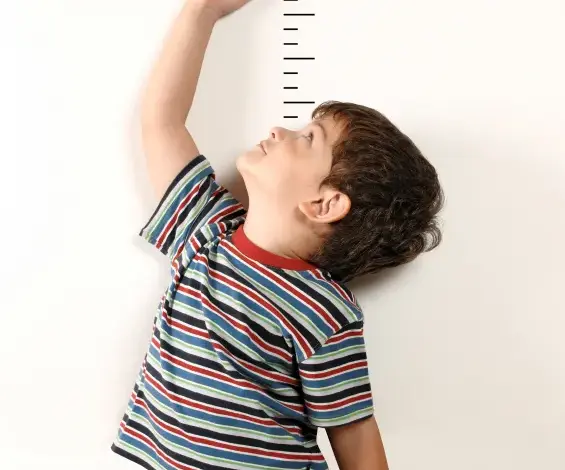 Chlapec měří svou výšku na růstové tabuli u zdi.
