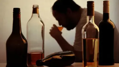 Muž pije alkohol mezi láhvemi, ilustrace závislosti.