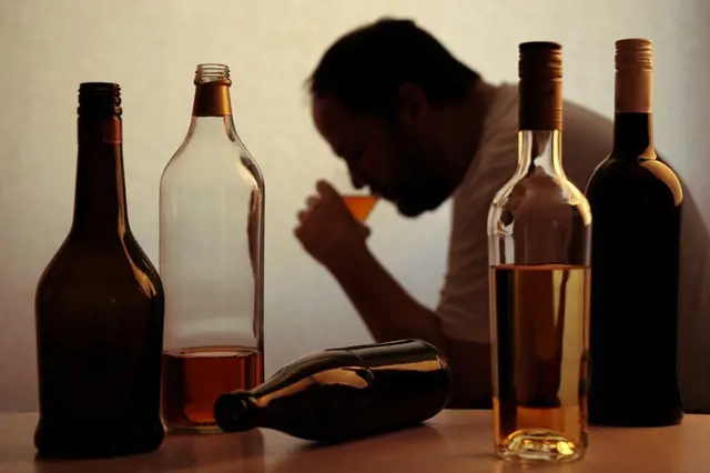 Muž pije alkohol mezi láhvemi, ilustrace závislosti.