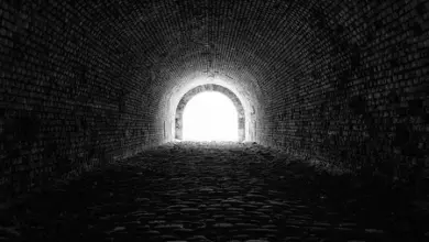Tmavá cihlová tunel s jasným světlem na konci.