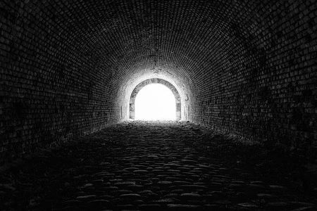 Tmavá cihlová tunel s jasným světlem na konci.