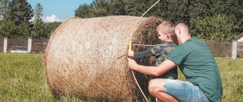 Muž pomáhá chlapci mířit na slámu s lukem.