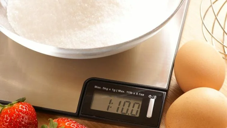 Digitální kuchyňská váha s cukrem v misce ukazuje hmotnost 110 gramů.