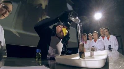 Student demonstruje chemický pokus před skupinou spolužáků.
