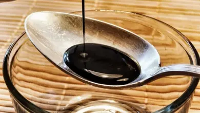 Tmavá tekutina se nalévá do polévkové lžíce nad skleněnou miskou.