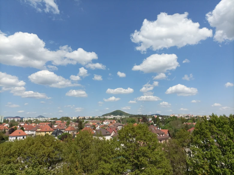 Pohled na město s domy, stromy a modrou oblohou.