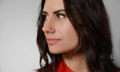 Žena s kroužkem v nose na neutrálním pozadí.