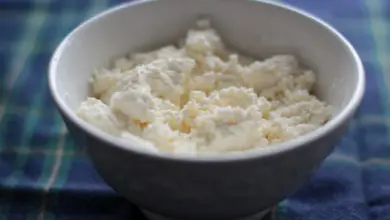 Bílá miska s tvarohem na modrém pruhovaném ubrusu.