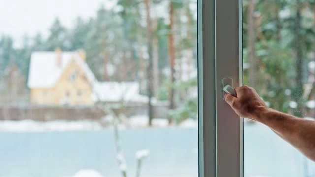 Ruka otevírá okno do sněhové krajiny venku.