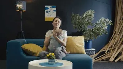 Žena sedí na modré pohovce s dítětem v náručí.