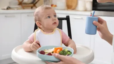 Babička krmití dítě zeleninou v jídelním křesle.