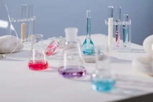 Laboratorní sklo s barevnými kapalinami na bílém povrchu.