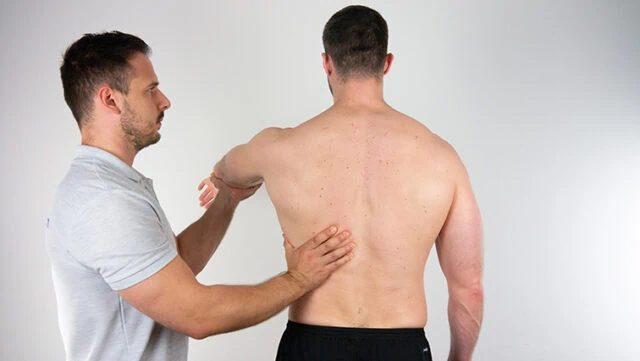 Fyzikální terapeut hmatá svalu latissimus dorsi u muže.