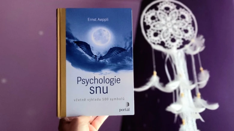 Ruka drží knihu o psychologii snů vedle bílého loveckého sítě.