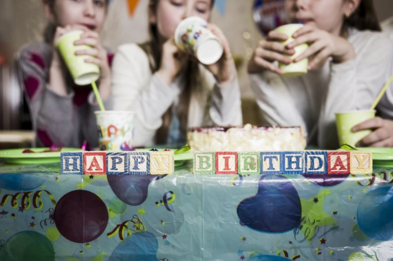 Dívky oslavují narozeniny s dortem a nápisem Happy Birthday na stole.