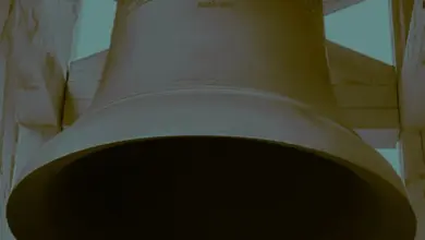 Velký kostelní zvon visící v dřevěném zvoniči s vyraženým nápisem.