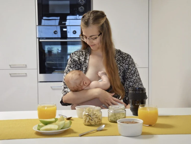Maminka kojí dítě u stolu s ovocem a zdravou stravou.