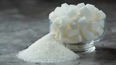 Skleněná miska s bílými kostkami cukru vedle hromádky granulovaného cukru.