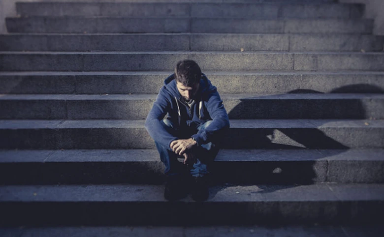 Smutný muž sedí na schodech v tmavém prostředí.