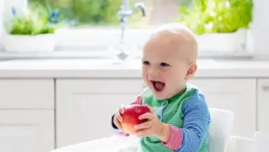 Šťastné dítě po roce sedící v židli s jablkem.