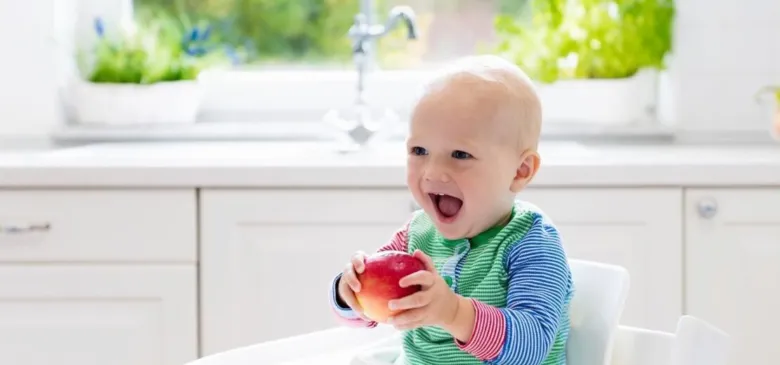 Šťastné dítě po roce sedící v židli s jablkem.