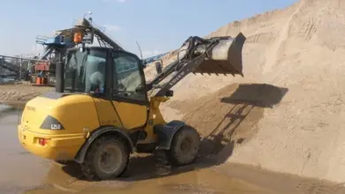 Žlutý nakladač s košem plným písku na lomu.