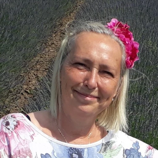Žena s květinou ve vlasech stojí mezi řadami levandule.