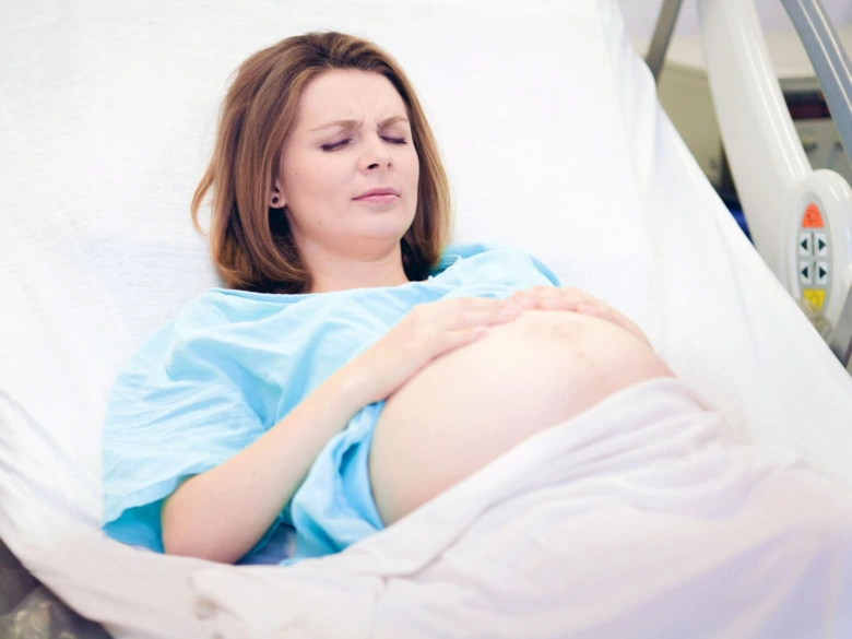 Těhotná žena v nemocničním lůžku s bolestivými kontrakcemi.
