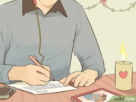 Muž píše dopis u svíčky s srdcem na stole.
