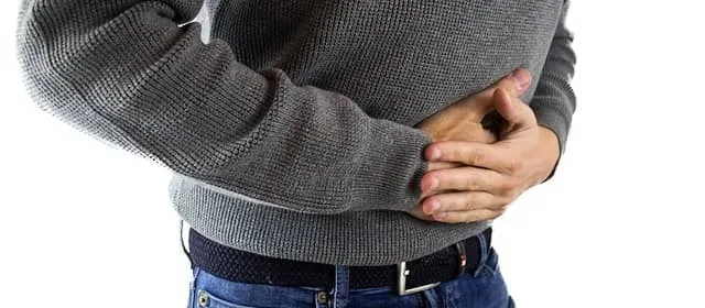 Muž drží břicho v bolesti po pití švestkového nápoje.