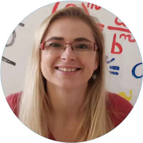 Portrétní fotografie ženy s brýlemi usmívající se před tabulí.