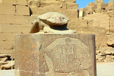 Kámenový sochařský skarabeus na podstavci před staroegyptskými ruinami.