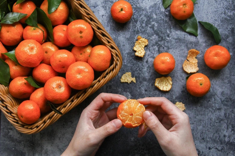 Ruce drží rozkrojený pomeranč vedle košíku plného citrusů.