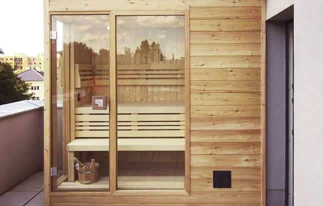 Sauna s dřevěnými lavicemi skleněnou přední stěnou na balkónu.