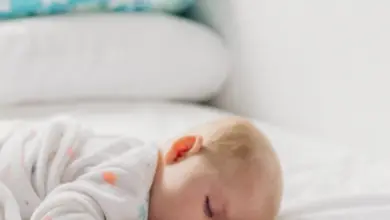 Spící dítě v posteli s modrým polštářem na pozadí.