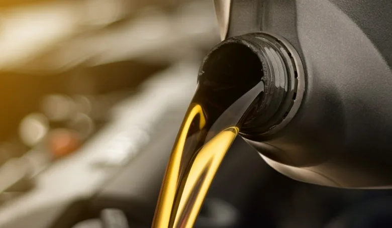 Zlatá olejová kapalina se lije z černé lahvičky do automobilového motoru.