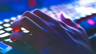 Ruce píšící na počítačové klávesnici s modrým osvětlením