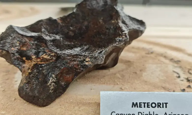 Meteorit z Arizony na pískovém podkladu s popisek.
