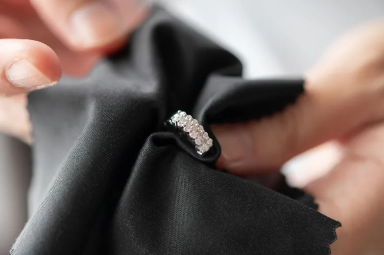 Ruka čistí prsten s diamanty černým mikrovláknovým utěrkou.