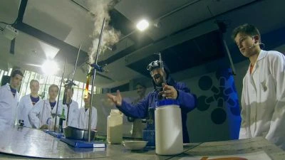 Skupina lidí v laboratoři pozoruje chemickou reakci s výfukem.