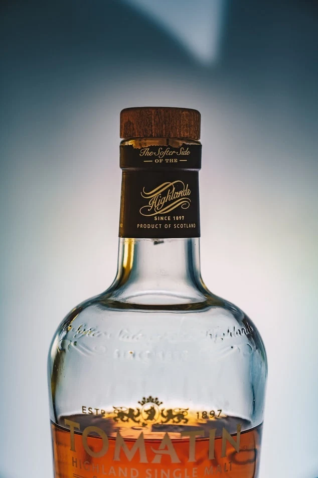 Hnědý whisky v lahví s dřevěným uzávěrem a zlatým štítkem.