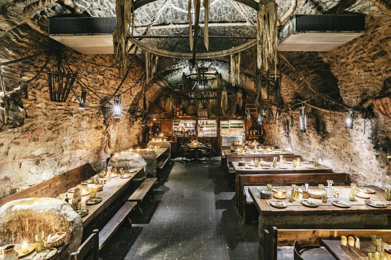 Interiér restaurace v jeskyni s dřevěnými stoly pro oslavy.