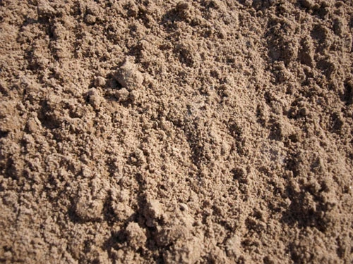 Zblízka viditelná textura písku s drobnými zrny a hrudkami.