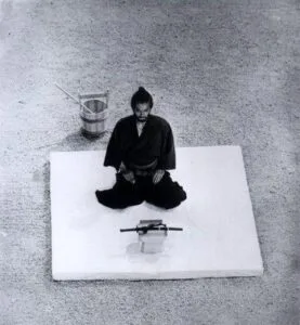 Samuraj sedící na podlaze s mečem pro rituální sebevraždu seppuku.