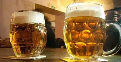 Dva sklenice piva s pěnou na dřevěném stole v hospodě.