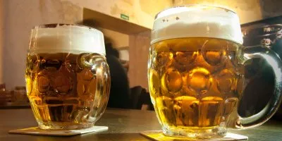 Dva sklenice piva s pěnou na dřevěném stole v hospodě.
