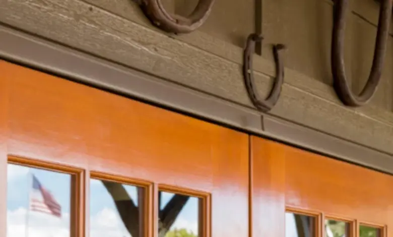 Rusty podkovy visí nad dřevěnými dveřmi s odrazem vlajky.