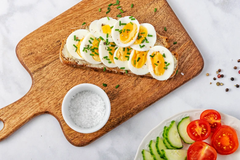 Uvařené vejce na toastu s bylinkami a solí vedle rajčat.